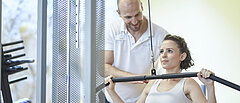 Medizinisches Training mit Trainier am Gewichthebegerät